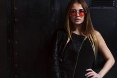 Façonnez la photo du modèle femelle attrayant dans les vêtements agressifs de style de roche et des lunettes de soleil roses posa photo stock Façonnez la photo du modèle femelle attrayant dans les vêtements agressifs de style de roche et des lunettes de soleil roses posa photo stock