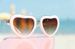 Façonnez les lunettes de soleil en forme de coeur sur le support rose avec le fond bleu de mer photos libres de droits Façonnez les lunettes de soleil en forme de coeur sur le support rose avec le fond bleu de mer photos libres de droits