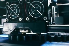 FDM 3D-printer manufacturing spur gears from silver-gray filament on blue print tape - front view on print head and nozzles stock photo FDM 3D-printer manufacturing spur gears from silver-gray filament on blue print tape - front view on print head and nozzles stock photo