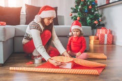 Feliz Natal e ano novo feliz Seriousand concentrou a mulher senta e cobre a caixa com o papel A menina pequena olha foto de stock royalty free Feliz Natal e ano novo feliz Seriousand concentrou a mulher senta e cobre a caixa com o papel A menina pequena olha foto de stock royalty free