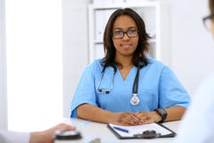 Female african american medical doctor with colleagues in background at hospital. Medicine and health care concept royalty free stock photo Female african american medical doctor with colleagues in background at hospital. Medicine and health care concept royalty free stock photo
