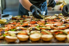 Female Chef Putting Ingredients of Burgers on a Sliced Bread Spread on a Table in Black Gloves - Concept of the Hard Working stock photography Female Chef Putting Ingredients of Burgers on a Sliced Bread Spread on a Table in Black Gloves - Concept of the Hard Working stock photography