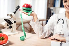 Female doctor sitting at desk in office with microscope and stethoscope. Woman is holding red apple with measuring tape. royalty free stock photography Female doctor sitting at desk in office with microscope and stethoscope. Woman is holding red apple with measuring tape. royalty free stock photography