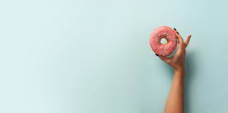 Female hand holding sweet donut over blue background. Top view, flat lay. Weight lost, sport, fitness, diet concept. Banner with royalty free stock photo Female hand holding sweet donut over blue background. Top view, flat lay. Weight lost, sport, fitness, diet concept. Banner with royalty free stock photo