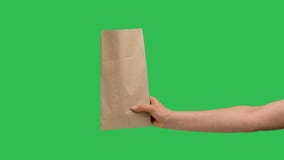 Female hand holds a paper shopping bag on the background of a green screen chroma key. Close up of paper packaging. Food
