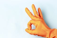 Female hand in orange rubber gloves shows ok sign, blue background royalty free stock image Female hand in orange rubber gloves shows ok sign, blue background royalty free stock image