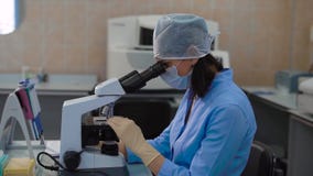 Female medical research assistant in blue lab coat working in laboratory and examining samples under the microscope stock video footage Female medical research assistant in blue lab coat working in laboratory and examining samples under the microscope stock video footage