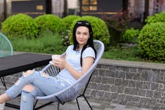 Female person sitting in chair at cafe near green plants and drinking coffee. Concept of leisure time and resting Royalty Free Stock Photo Female person sitting in chair at cafe near green plants and drinking coffee. Concept of leisure time and resting Royalty Free Stock Photo
