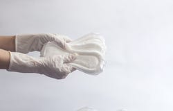 Female`s hygiene products. Woman`s hands in medical gloves holding a stack of sanitary napkins against white background. Period stock images Female`s hygiene products. Woman`s hands in medical gloves holding a stack of sanitary napkins against white background. Period stock images