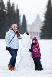 Femme adulte heureuse et souriante et jeune fille tenant le bonhomme de neige proche sur le champ hivernal du parc, horaire d'hiv photo stock Femme adulte heureuse et souriante et jeune fille tenant le bonhomme de neige proche sur le champ hivernal du parc, horaire d'hiv photo stock