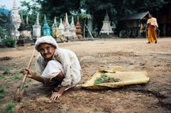 femme agée nettoyant l'arrière-cour d'un monastère tandis qu'un moine passe par à l'arrière-plan devant beaucoup de petits stupas image stock femme agée nettoyant l'arrière-cour d'un monastère tandis qu'un moine passe par à l'arrière-plan devant beaucoup de petits stupas image stock