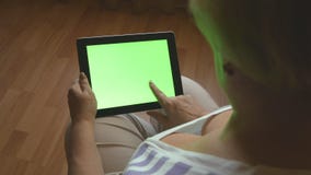 Femme agée s'asseyant sur le sofa à la maison et à l'aide d'un PC numérique de comprimé avec l'écran vert, vue arrière Tablette d banque de vidéos Femme agée s'asseyant sur le sofa à la maison et à l'aide d'un PC numérique de comprimé avec l'écran vert, vue arrière Tablette d banque de vidéos