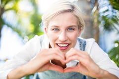 Femme assez blonde souriant à l'appareil-photo et faisant la forme de coeur avec ses mains Photographie stock Femme assez blonde souriant à l'appareil-photo et faisant la forme de coeur avec ses mains Photographie stock