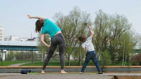 Femme avec son fils faisant le yoga par l'?tang, dehors clips vidéos Femme avec son fils faisant le yoga par l'?tang, dehors clips vidéos