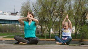 Femme avec son fils faisant le yoga par l'étang, dehors clips vidéos Femme avec son fils faisant le yoga par l'étang, dehors clips vidéos