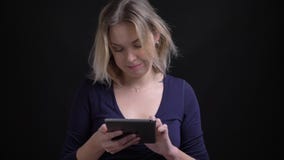 Femme d'affaires blonde dans le chemisier bleu observant avec l'intérêt positif dans le comprimé au fond noir clips vidéos Femme d'affaires blonde dans le chemisier bleu observant avec l'intérêt positif dans le comprimé au fond noir clips vidéos