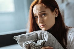 Femme d'une chevelure rouge triste tenant un coussin photographie stock libre de droits Femme d'une chevelure rouge triste tenant un coussin photographie stock libre de droits