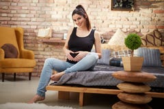 Femme enceinte heureuse s'asseyant sur le lit à la maison photo libre de droits Femme enceinte heureuse s'asseyant sur le lit à la maison photo libre de droits