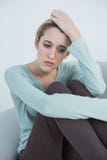 Femme réfléchie attirante s'asseyant sur le divan photo libre de droits Femme réfléchie attirante s'asseyant sur le divan photo libre de droits