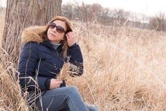 Femme s'asseyant contre l'arbre dans le domaine tenant le wildflo sélectionné frais photo stock Femme s'asseyant contre l'arbre dans le domaine tenant le wildflo sélectionné frais photo stock