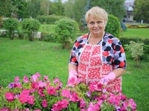 Femme supérieure heureuse enfilée de gants dans le jardin montrant les fleurs colorées photographie stock libre de droits Femme supérieure heureuse enfilée de gants dans le jardin montrant les fleurs colorées photographie stock libre de droits