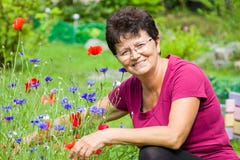 Femme supérieure positive s'asseyant parmi des fleurs dans un jardin photo stock Femme supérieure positive s'asseyant parmi des fleurs dans un jardin photo stock