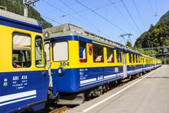 Fermate ferroviarie gialle e blu del treno di Bernese Oberland al binario della stazione ferroviaria di Grindelwald fotografia stock libera da diritti Fermate ferroviarie gialle e blu del treno di Bernese Oberland al binario della stazione ferroviaria di Grindelwald fotografia stock libera da diritti