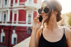 Fermez-vous de la femme caucasienne attirante gaie avec les cheveux foncés dans les lunettes de soleil et la robe noire parlant a image libre de droits Fermez-vous de la femme caucasienne attirante gaie avec les cheveux foncés dans les lunettes de soleil et la robe noire parlant a image libre de droits