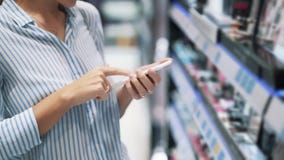 Fermez-vous de la femme que les mains utilise le téléphone dans le magasin cosmétique, mouvement lent banque de vidéos Fermez-vous de la femme que les mains utilise le téléphone dans le magasin cosmétique, mouvement lent banque de vidéos