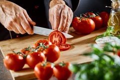 Fermez-vous sur l'homme découpant en tranches vers le haut de petites tomates photo libre de droits Fermez-vous sur l'homme découpant en tranches vers le haut de petites tomates photo libre de droits