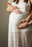Fermez-vous vers le haut de la photo de la femme enceinte dans la robe blanche élégante touchant son ventre avec des mains de fem Photographie stock Fermez-vous vers le haut de la photo de la femme enceinte dans la robe blanche élégante touchant son ventre avec des mains de fem Photographie stock