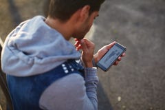 Fermez-vous vers le haut du jeune homme beau à l'aide du téléphone intelligent tout en se tenant dehors à la soirée ensoleillée photo stock Fermez-vous vers le haut du jeune homme beau à l'aide du téléphone intelligent tout en se tenant dehors à la soirée ensoleillée photo stock