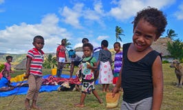 A Fijian young child in Navala, Fiji smiling looking into the camera with his fellow villagers behind
