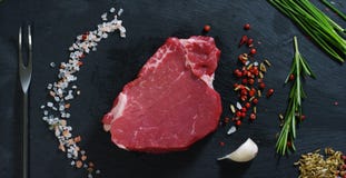 Filete jugoso hermoso de la carne fresca en una tabla con la sal, el romero, el ajo, y el tomate en un fondo negro, visión superi imágenes de archivo libres de regalías Filete jugoso hermoso de la carne fresca en una tabla con la sal, el romero, el ajo, y el tomate en un fondo negro, visión superi imágenes de archivo libres de regalías