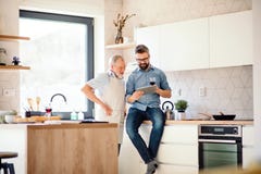 Filho adulto do moderno e pai superior dentro na cozinha em casa, usando a tabuleta fotos de stock Filho adulto do moderno e pai superior dentro na cozinha em casa, usando a tabuleta fotos de stock