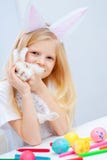 Fille blonde dans des oreilles de lapin sur la tête et petit lapin dans des ses mains Oeufs et marqueurs colorés sur la table Pre images libres de droits Fille blonde dans des oreilles de lapin sur la tête et petit lapin dans des ses mains Oeufs et marqueurs colorés sur la table Pre images libres de droits