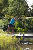 Fille blonde décontractée s'étirant sur un pont en bois et une eau photo libre de droits Fille blonde décontractée s'étirant sur un pont en bois et une eau photo libre de droits