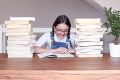 Fille de sourire heureuse mignonne de tween en verres étudiant le livre de lecture reposant une table avec la pile des livres à l photo libre de droits Fille de sourire heureuse mignonne de tween en verres étudiant le livre de lecture reposant une table avec la pile des livres à l photo libre de droits
