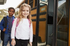 Fille et garçon d'école primaire attendant pour monter à bord de l'autobus scolaire image stock Fille et garçon d'école primaire attendant pour monter à bord de l'autobus scolaire image stock