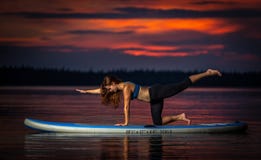 Fille exerçant le yoga sur le paddleboard dans le coucher du soleil sur le lac scénique Velke Darko image libre de droits Fille exerçant le yoga sur le paddleboard dans le coucher du soleil sur le lac scénique Velke Darko image libre de droits
