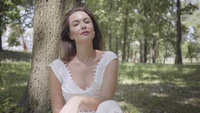 Fille fascinante de portrait jeune avec de longs cheveux de brune portant une longue robe blanche de mode d'été se reposant sous banque de vidéos Fille fascinante de portrait jeune avec de longs cheveux de brune portant une longue robe blanche de mode d'été se reposant sous banque de vidéos