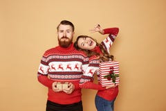 Fille heureuse et un type habillé dans des chandails rouges et blancs avec des cadeaux de Noël de prise de cerfs communs dans leu photo stock Fille heureuse et un type habillé dans des chandails rouges et blancs avec des cadeaux de Noël de prise de cerfs communs dans leu photo stock