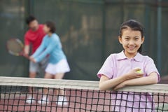 fille se tenant à côté du filet de tennis, parents jouant à l'arrière-plan photographie stock fille se tenant à côté du filet de tennis, parents jouant à l'arrière-plan photographie stock