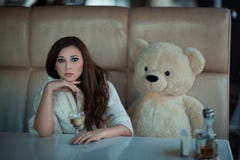 Fille triste à la table avec un ours de jouet images stock Fille triste à la table avec un ours de jouet images stock