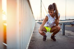 Fille urbaine de sport avec des écouteurs se reposant sur le pont dans le coucher du soleil photo libre de droits Fille urbaine de sport avec des écouteurs se reposant sur le pont dans le coucher du soleil photo libre de droits