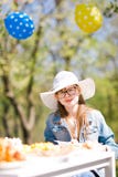 Fille âgée de l'adolescence dans le chapeau de soleil blanc se reposant par la table sur l'anniversaire le Gard photographie stock libre de droits Fille âgée de l'adolescence dans le chapeau de soleil blanc se reposant par la table sur l'anniversaire le Gard photographie stock libre de droits