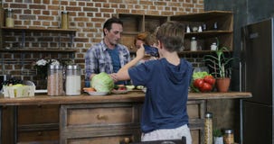 Fils faisant la vidéo de la famille heureuse dans la cuisine faisant cuire le repas de préparation de sourire heureux de nourritu clips vidéos Fils faisant la vidéo de la famille heureuse dans la cuisine faisant cuire le repas de préparation de sourire heureux de nourritu clips vidéos