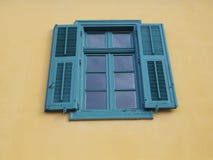 Finestra con gli otturatori blu o verdi su una parete gialla immagini stock Finestra con gli otturatori blu o verdi su una parete gialla immagini stock