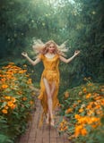 Fiore attraente misterioso leggiadramente in vestito giallo-chiaro con il treno lungo e le gambe aperte nel salto nella foresta c immagine stock Fiore attraente misterioso leggiadramente in vestito giallo-chiaro con il treno lungo e le gambe aperte nel salto nella foresta c immagine stock
