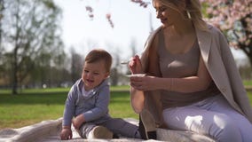 Fiore di ciliegia di Sakura - giovane madre della mamma che si siede con suo figlio del bambino del ragazzino in un parco a Riga, stock footage Fiore di ciliegia di Sakura - giovane madre della mamma che si siede con suo figlio del bambino del ragazzino in un parco a Riga, stock footage